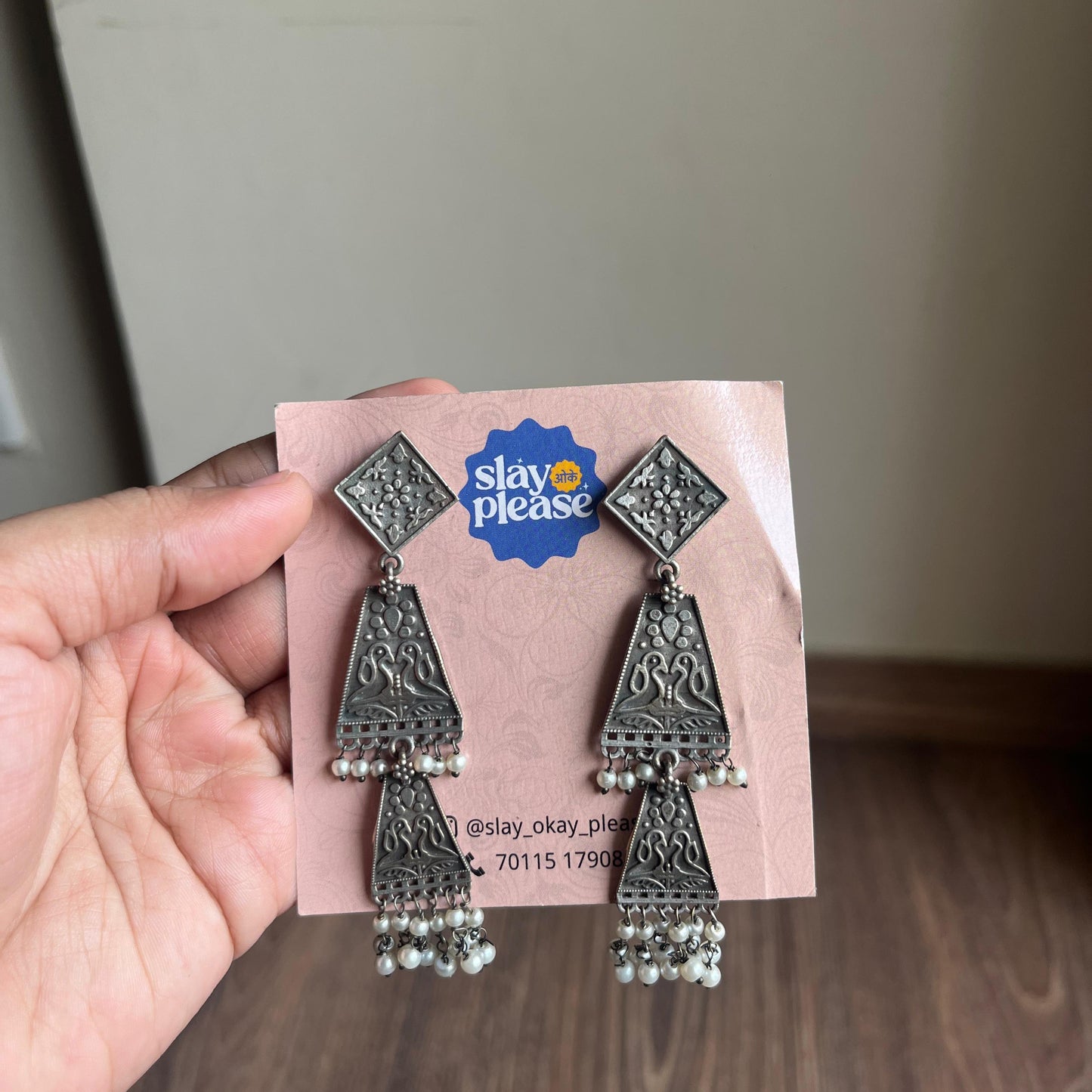 Silver earrings on a 'Slay Okay Please' branded card held by a hand.