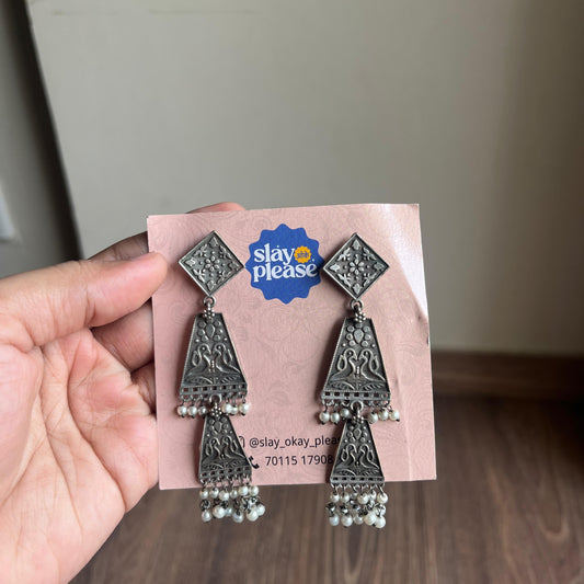 Silver earrings on a 'Slay Okay Please' branded card held by a hand.