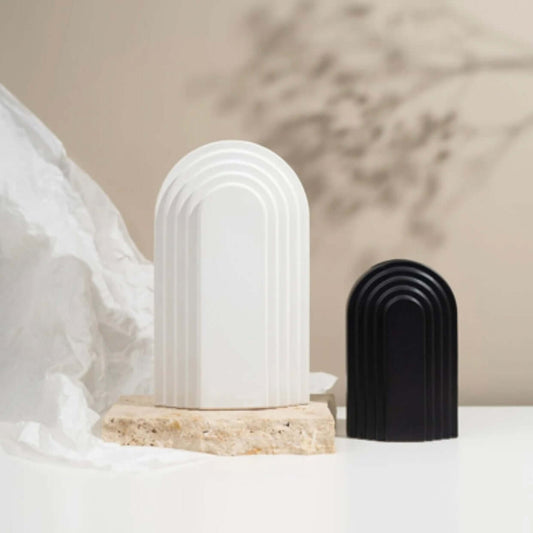 Two arch-shaped ceramic objects, one white and one black, on a neutral background.
