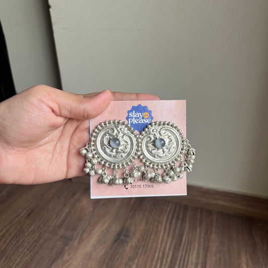 Hand holding a pair of silver earrings on a pink card with 'Please' text.