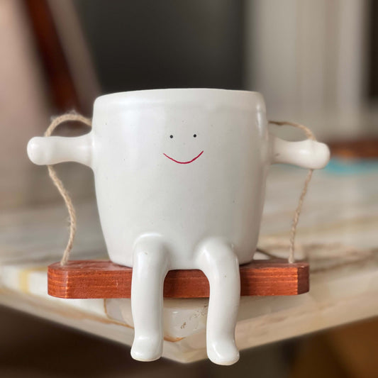 White ceramic planter with smiley face and legs on a wooden stand