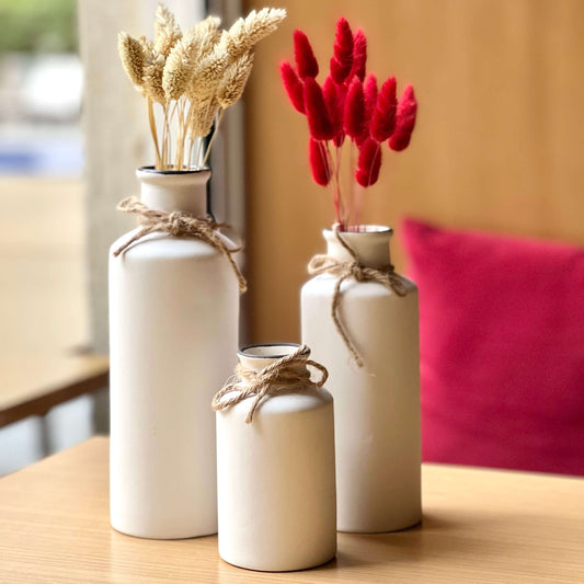 Three white vases with decorative dried flowers on a wooden surface