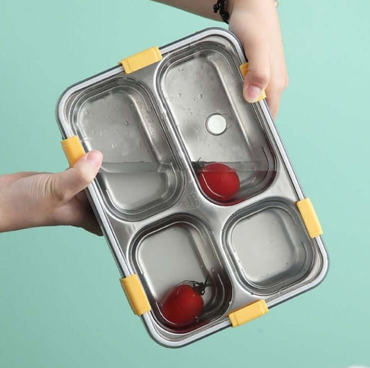 Stainless steel compartmentalized food container with yellow lids held by a person against a light blue background